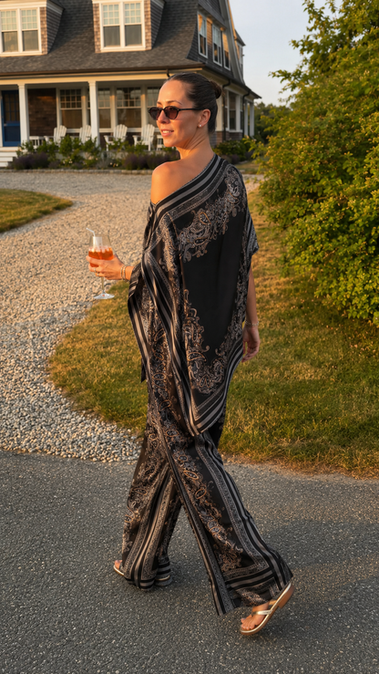 Model wearing black printed draped poncho top with matching wide leg pants side view