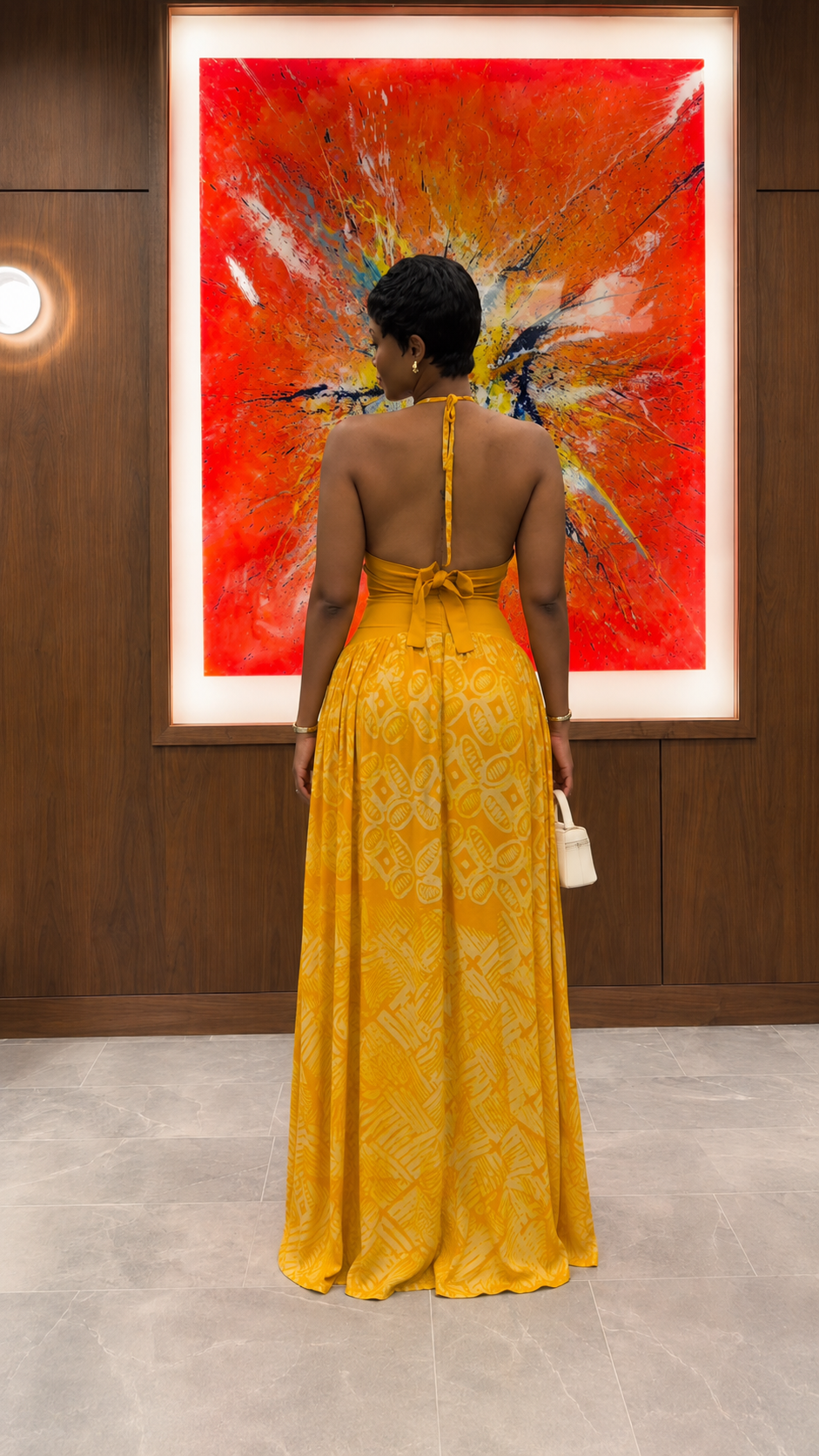 Back view of mustard halter neck maxi dress with tie-back detail and open upper back